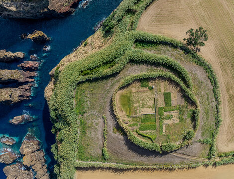 Aerial view of the circular Miradouro da Vigia agricultural plot enclosed by tall green hedges on a cliff edge overlooking the Atlantic Ocean in Capelas, Azores, Portugal.