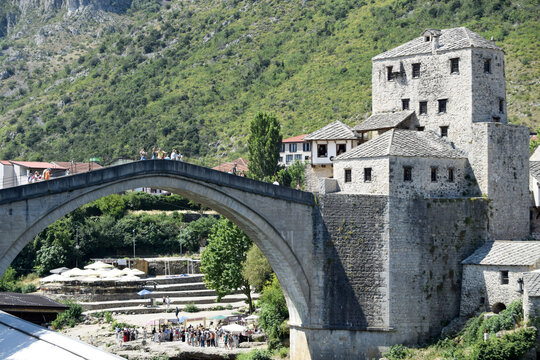 View of the historic Stari Most stone arch bridge with people walking across it and stone buildings in the background in Mostar, Federation of Bosnia, Bosnia and Herzegovina.