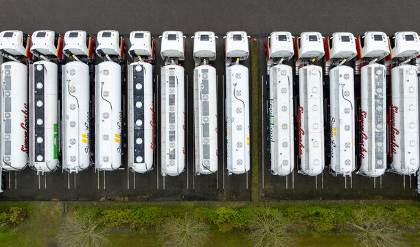 Wognum, Noord-Holland, Netherlands - 27 April 2024: Aerial view of a fleet of white tanker trucks parked in neat rows at a logistics facility.