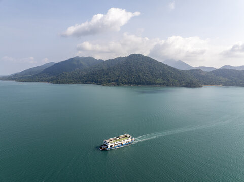 Aerial view of the Koh Chang Ferry crossing the turquoise waters of the Gulf of Thailand with lush green mountains in the background in Khlong Yai, Trat, Thailand.