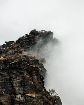 View of Fanjing Shan temple perched on a rocky mountain peak surrounded by thick mist and clouds in Tongren, China.