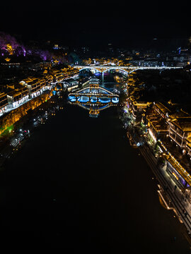 Aerial view of the illuminated Fenghuang Ancient Town with traditional architecture reflecting in the Tuojiang River, Fenghuang, Hunan, China.