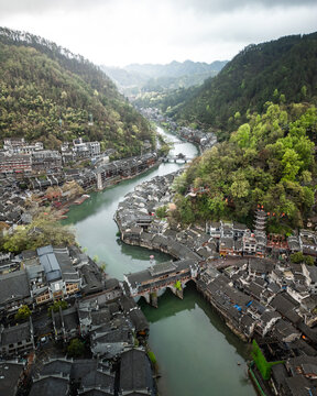 Aerial view of Fenghuang Ancient Town with traditional stilt houses along the Tuojiang River, surrounded by lush mountains in Xiangxi Tujia and Miao Autonomous Prefecture, Hunan, China.