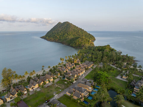 Aerial view of Little Sunshine Resort nestled along the coastline with tropical palm trees, swimming pools, and a lush green mountain backdrop in Klong son, Chang Wat Trat, Thailand.