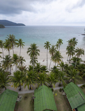 Aerial view of Haad Khlong Hin Beach with lush palm trees, white sand, and turquoise water under a cloudy sky in Ko Kut, Thailand.