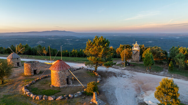 Aerial view of Moinhos de Portela de Oliveira, featuring traditional stone windmills at sunset with a surrounding forest landscape in Sazes do Lorvao, Coimbra, Portugal.