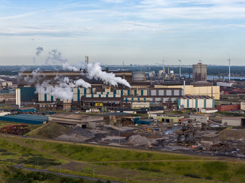 Velsen-Noord, Netherlands - 06 July 2026: Aerial view of the Tata Steel plant with industrial buildings, smoking chimneys, and surrounding storage yards under a clear sky.