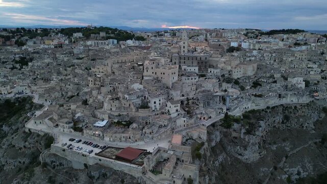 Aerial view of the ancient Sassi di Matera with historic stone dwellings, narrow streets, and rocky cliffs at dusk in Italy.