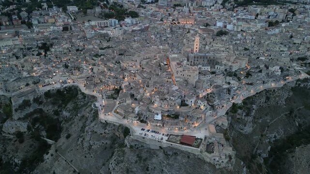 Aerial view of the historic Sassi di Matera, an ancient cave dwelling district carved into the limestone cliffs, illuminated at dusk in Italy.
