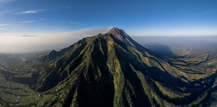 Aerial view of Mount Merapi near New Selo, featuring volcanic slopes, lush vegetation, and agricultural terraces in the valley. Kecamatan Selo, Jawa Tengah, Indonesia.