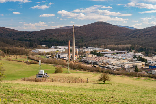 Aerial view of the PPS GROUP a.s. industrial facility with its prominent chimney set against a backdrop of rolling hills and green fields in Viglas, Banskobystricky kraj, Slovakia.