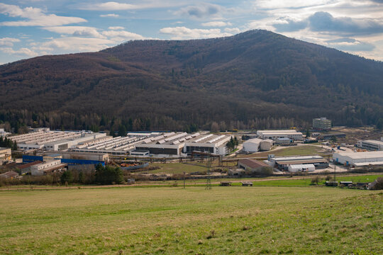 Aerial view of PPS Group a.s. industrial facility nestled at the foot of a forested mountain with factory buildings, warehouses, and surrounding green fields in Viglas, Banskobystricky kraj, Slovakia.