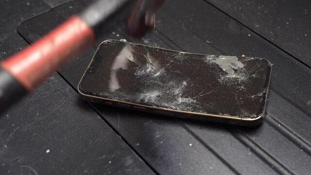 Hammer smashing a smartphone screen on a black table, concept of technology stress and anger