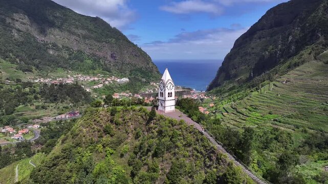 Aerial view of the Chapel of Our Lady of Fatima situated on a lush green hill overlooking the coastal village and the Atlantic Ocean in Madeira.