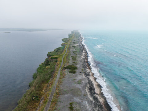 Aerial view of the Pomorie sandbar separating the Black Sea from the Pomorie Lake with a narrow path and coastal vegetation in Pomorie, Burgas, Bulgaria.