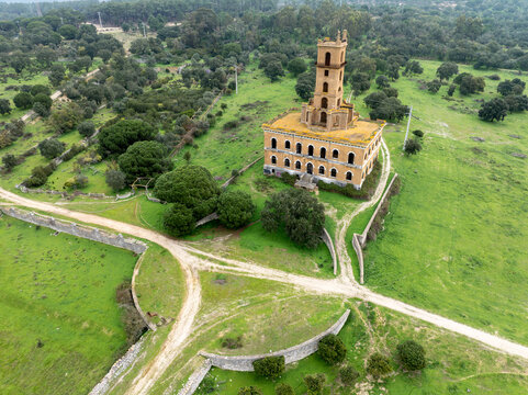 Aerial view of the historic Castelo do Rei do Lixo, an abandoned palace with a prominent tower, surrounded by green fields, trees, and dirt paths in Coina, Setubal, Portugal.