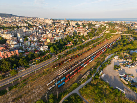 Aerial view of the southern industrial zone in Varna featuring long freight trains on multiple tracks, adjacent to urban residential buildings in Varna, Varna, Bulgaria.