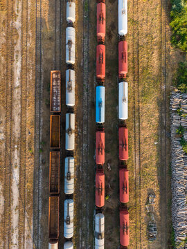 Aerial view of colorful freight train cars parked on parallel tracks in the southern industrial zone with dry grass and timber stacks in Varna, Varna, Bulgaria.