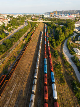 Aerial view of the southern industrial zone in Varna with freight trains on parallel tracks, surrounded by lush green trees and urban infrastructure in Varna, Varna, Bulgaria.