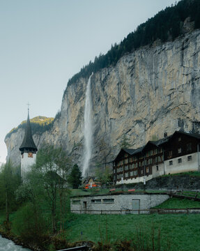 View of the iconic Staubbach Falls cascading down a sheer cliff face beside a traditional church and wooden houses in the Lauterbrunnen valley, Switzerland.