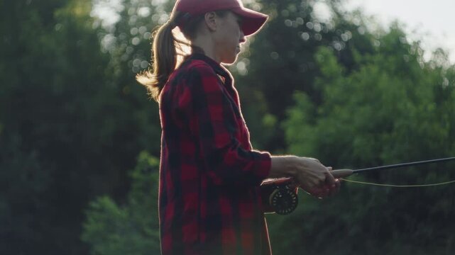 Young woman fly fishing on the small shallow river during summer day