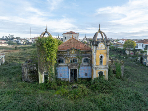 Aerial view of the abandoned Quinta Conde de Sucena mansion with its distinctive towers, tiled facade, and overgrown vegetation in Borralha, Aveiro, Portugal.
