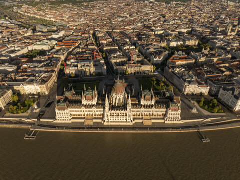 Aerial view of the Hungarian Parliament Building situated on the banks of the Danube River, surrounded by the dense urban architecture of Budapest, Hungary.