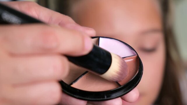 Close-up of a woman applying blush to her cheek with a soft makeup brush. Beauty routine, cosmetics, facial makeup and skincare concept