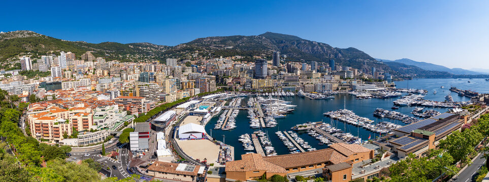 View of the bustling Port Hercules harbor filled with luxury yachts, surrounded by the dense urban architecture and hills of Monaco City, Monaco.