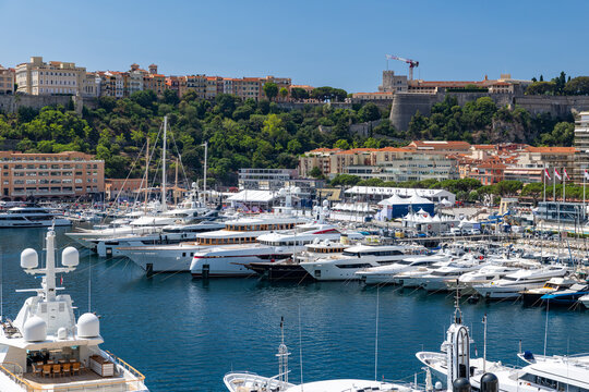 View of Port Hercules filled with luxury yachts and boats against the backdrop of historic buildings and lush hillside in Monaco City, Monaco.
