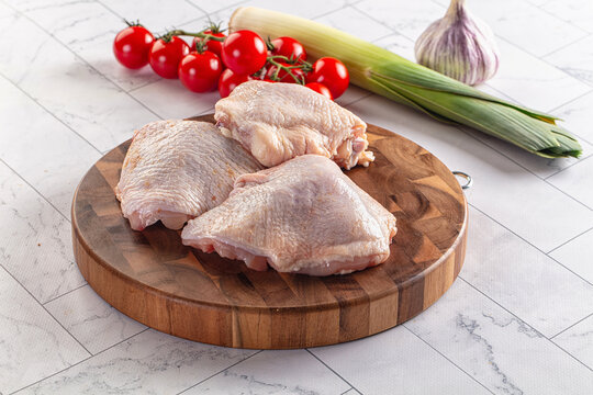 Raw chicken thighs on wooden cutting board with cherry tomatoes leek and garlic