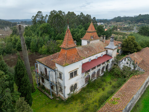 Aerial view of the abandoned Ruinas Quinta da Zombaria with its distinctive red tiled towers and overgrown grounds surrounded by lush forest in Antuzede e Vil de Matos, Coimbra, Portugal.