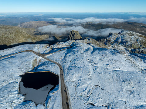 Aerial view of Lago da barragem da Torre in the snow-covered Serra da Estrela mountains, featuring a winding road and a frozen lake in Manteigas, Distrito da Guarda, Portugal.