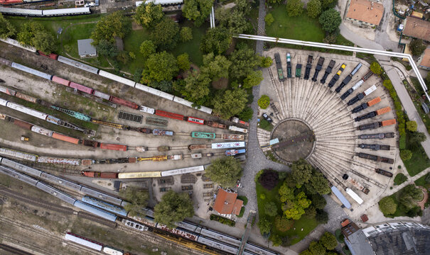 Aerial view of the Hungarian Railway Museum featuring a historic roundhouse with a central turntable and vintage locomotives parked on radiating tracks surrounded by greenery in Budapest, Hungary.