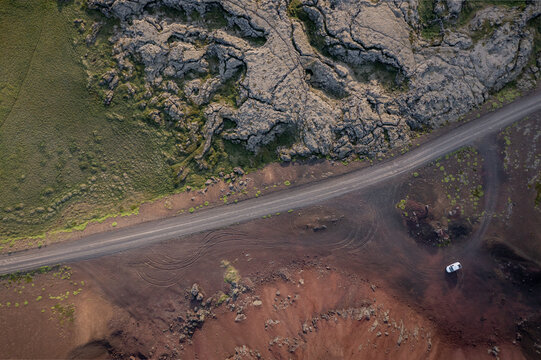 Aerial view of Ytri-Raudarmelskula volcanic crater with rugged lava fields, a winding road, and a car parked nearby in Raudhamelur, Eyja- og Miklaholtshr, Iceland.