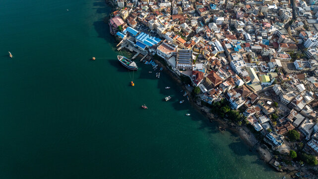 Aerial view of the historic coastal city of Mombasa, featuring dense urban architecture and small boats anchored in the turquoise waters of the Indian Ocean, Mombasa, Mombasa County, Kenya.