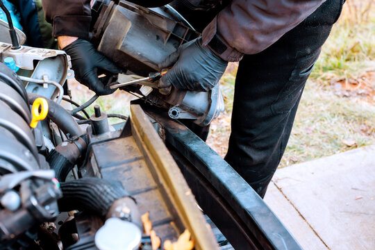 Service worker repairs car headlight, by removing an old part in an outdoor garage setting