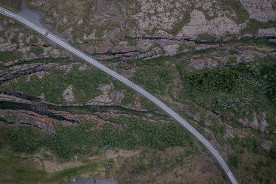 Aerial view of Thingvellir National Park showing a road winding through rugged volcanic fissures and green mossy terrain in Selfoss, Blaskogabyggd, Iceland.