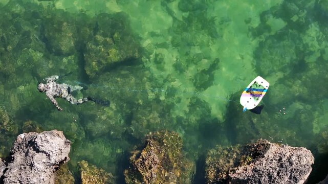 Aerial view of a scuba diver swimming in clear turquoise water near rocky formations with a float in Cascais, Lisbon, Portugal.
