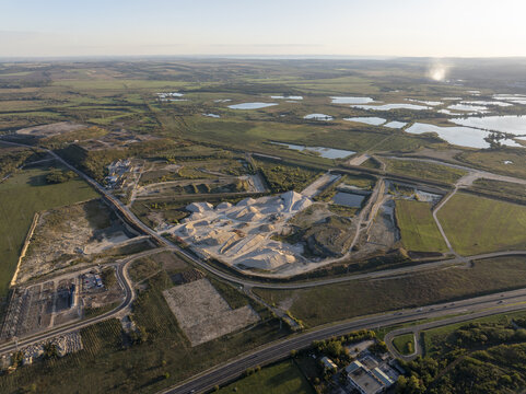 Aerial view of the abandoned Inota Power Plant cooling towers surrounded by industrial gravel piles, ponds, and green fields near a highway in Varpalota, Hungary.