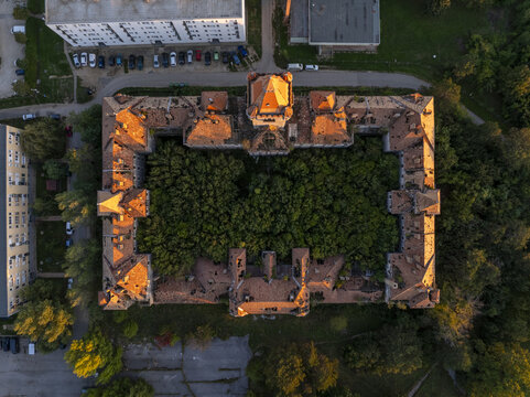 Aerial view of the abandoned Hajmasker Barracks, featuring a large rectangular building with orange-tiled roofs and a dense forest growing within its central courtyard. Hajmasker, Hungary.