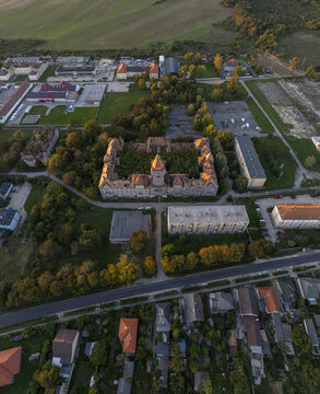 Aerial view of the historic Hajmasker Barracks featuring a prominent central tower and surrounding lush trees, set amidst residential buildings and green fields in Hajmasker, Hungary.