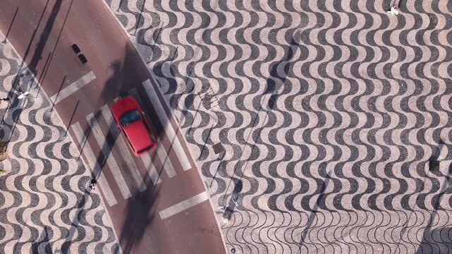 Aerial view of a person walking across a pedestrian crossing on traditional Portuguese mosaic pavement with a wave pattern in Cascais, Lisbon, Portugal.