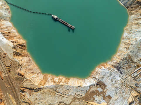 Aerial view of a dredging vessel floating in a turquoise mining pond surrounded by excavated sand and earth banks in Coimbra, Coimbra District, Portugal.