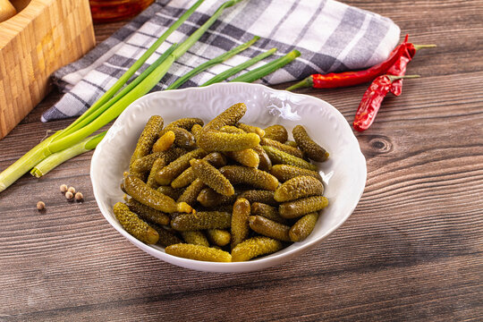 Pickled gherkins in white bowl with green onions and red chili peppers on wooden table