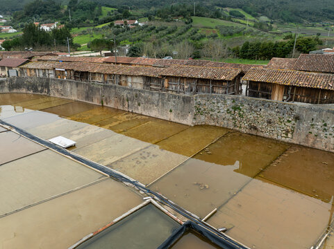 Aerial view of Salinas de Rio Maior salt pans with traditional wooden storage buildings, stone walls, and evaporation ponds in the rural landscape of Rio Maior, Santarem, Portugal.