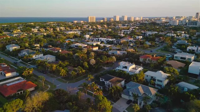 Aerial view of a residential neighborhood with lush trees, suburban houses, and streets, with the distant coastline and ocean visible in Boca Raton, Florida, United States.