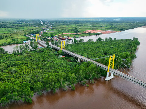 Aerial view of Barito Bridge spanning the Barito River, surrounded by lush green tropical forests and mangroves in Kecamatan Alalak, Kalimantan Selatan, Indonesia.