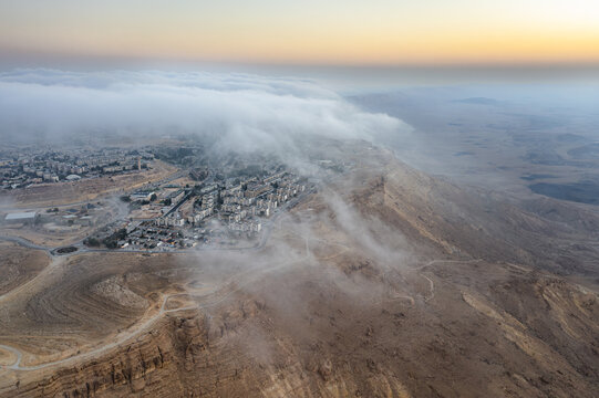 Aerial view of the Mitzpe Ramon crater rim with low-hanging clouds rolling over the town of Mitzpe Ramon in the Negev desert, Mitzpe Ramon, South District, Israel.