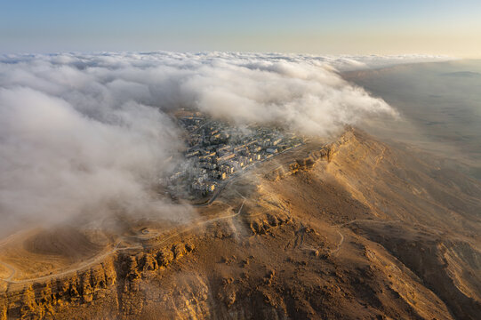 Aerial view of Mitzpe Ramon town situated on the edge of the Makhtesh Ramon crater with clouds rolling over the desert landscape during golden hour in Mitzpe Ramon, South District, Israel.